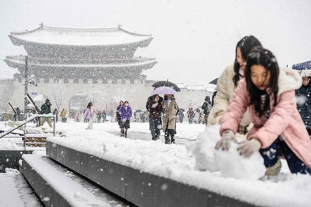 2024年11月27日，首尔市中心大雪纷飞，行人走在景福宫前，孩子在堆雪人。视觉中国 图