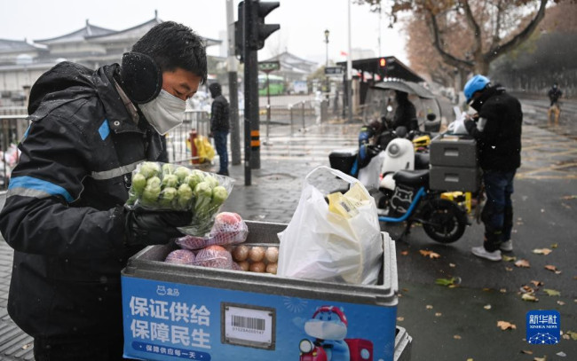 12月25日，外卖人员张欣（左一）在西安市小寨东路一封控小区配送蔬菜。这几天，他的业务量是平时的两倍。