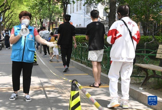 5月5日，在北京市海淀区中关村街道东里南社区临时核酸检测采样点，社区工作人员（左一）引导市民有序排队。