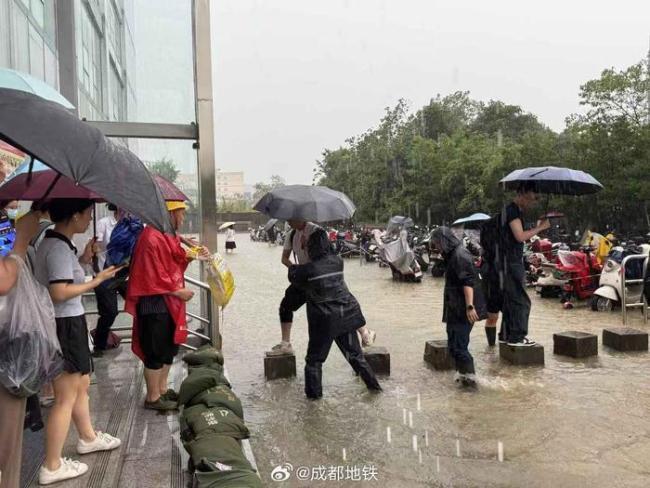 成都地铁口工作人员为乘客发雨衣 暴雨中搭“便桥”护送安全出行
